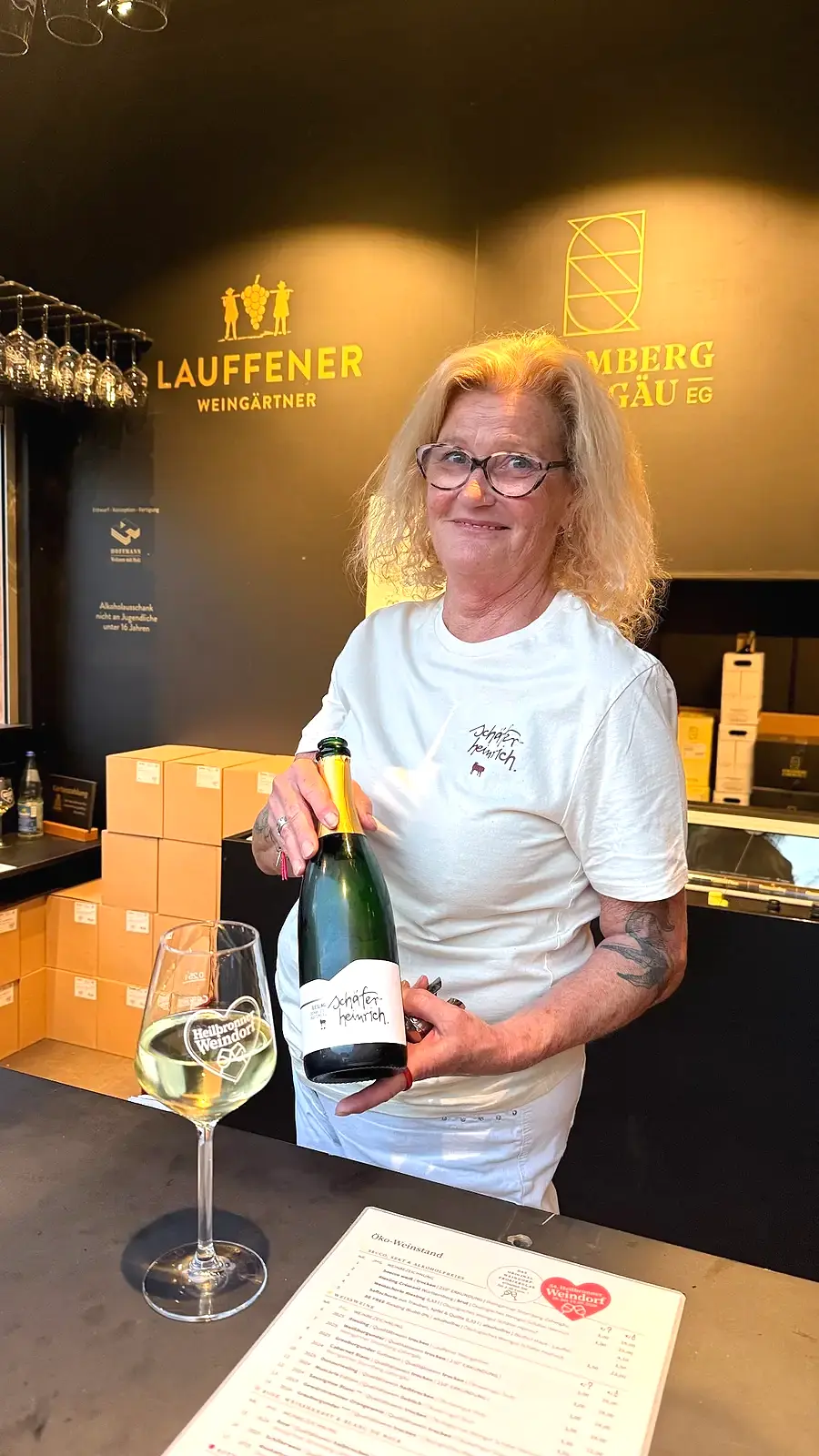 Winzerin mit Weinflasche und Weindorfglas an einem Stand des Heilbronner Weindorfs